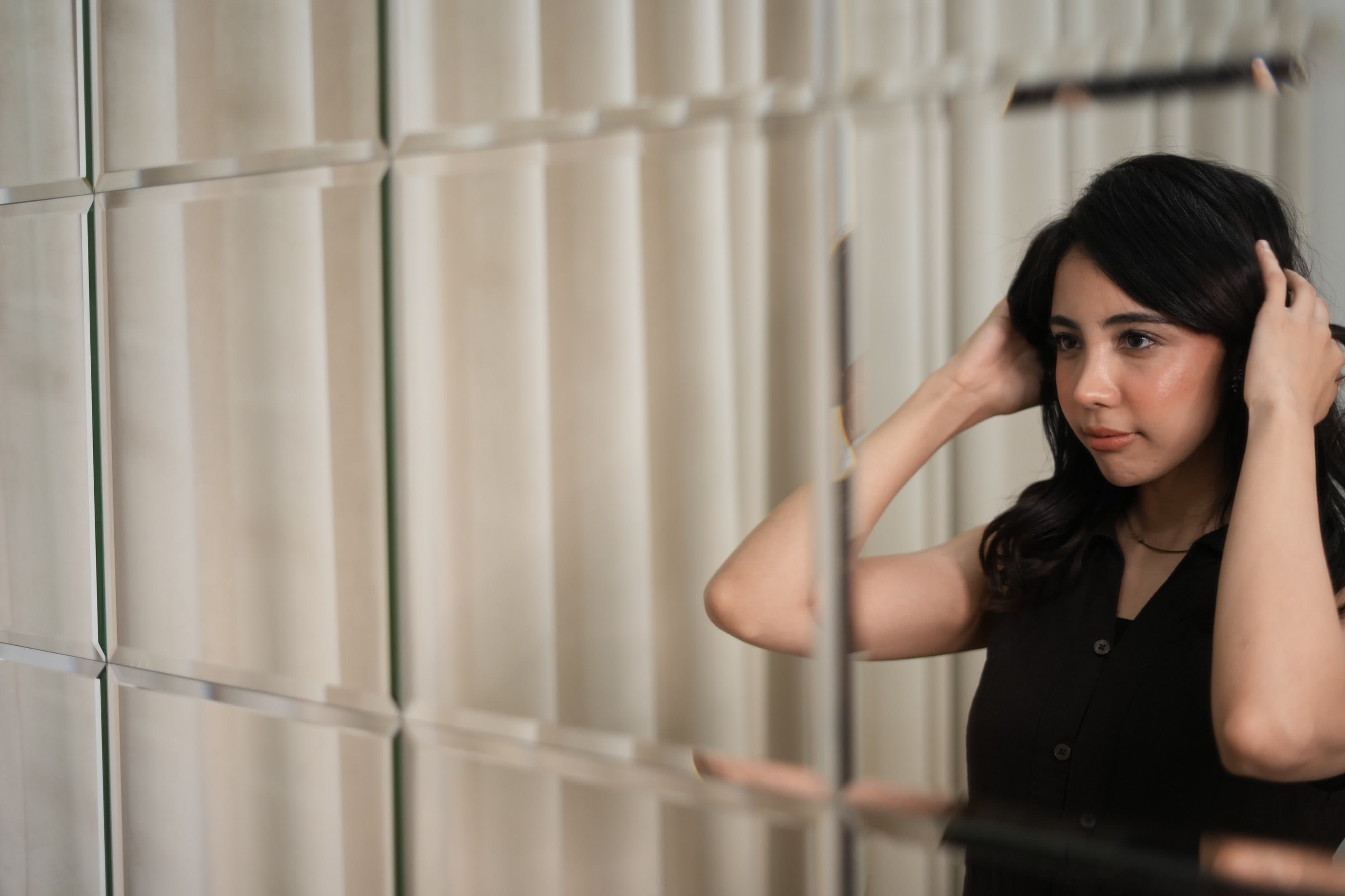 Client adjusting her finished hairstyle in a fragmented salon mirror.